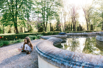 A sad child sits alone by a fountain in a park