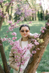 a woman dressed in a spring jacket, pants and sunglasses poses exquisitely against the background...