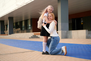 mother and daughter embrace outdoors with school backdrop, showcasing parent-child bond and back-to-school theme. happy expressions reflect warmth, love, and supportive relationship