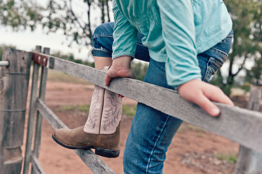 Tween girl climbing a timber fence on a rural property