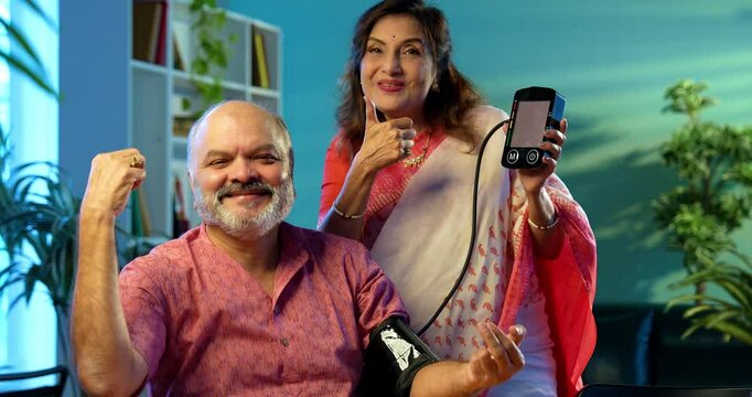 Senior couple measuring blood pressure at home using digital BP monitor sitting together at the table, Indian retired family happy with healthy readings, wellness, aging, healthcare lifestyle concept
