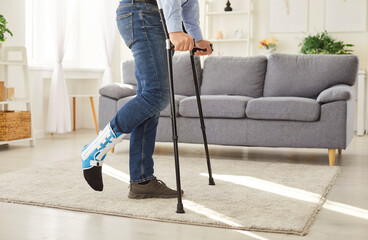 Cropped photo of disabled young man with broken leg after accident using crutches standing in...