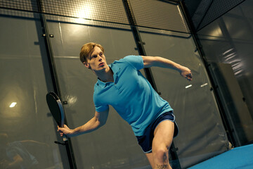 Young sportsman showcases impressive skills during a padel match in an indoor court