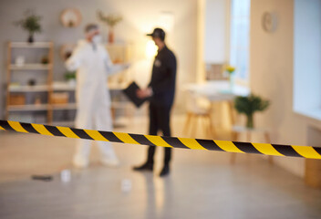 Blurred view of forensic investigator and police officer discussing evidence behind caution tape....