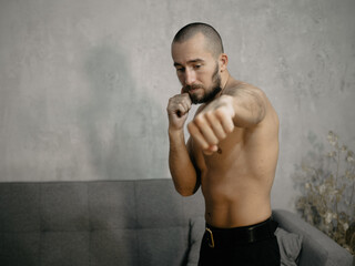 A young attractive man trains boxing at home after work.