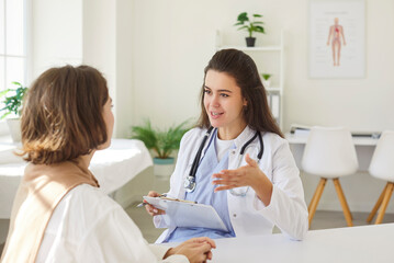 Young nurse, smiling female doctor consulting woman patient at appointment in clinic, explaining...