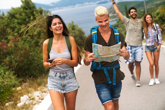 Happy friends on a road trip have fun, piggybacking at the roadside and enjoying summer vacation