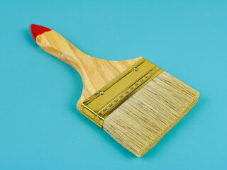 A wide, clean paint brush with wooden handle on teal background.