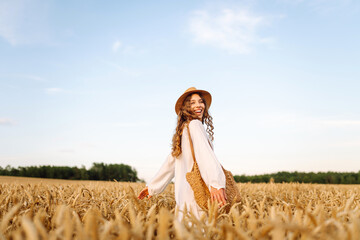 Obraz premium Joyful woman in white dress posing in golden wheat field. Young woman having fun and enjoying sunny weather outdoors. Nature and enjoyment concept.