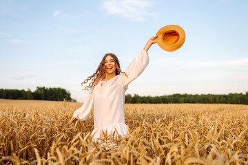 Joyful woman in white dress posing in golden wheat field. Young woman having fun and enjoying sunny...