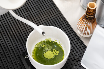 Barista making macha green tea in to white cup at the coffee shop.Close-up of four white kettles while preparing matcha menu from green tea powder on black background.