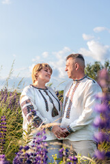 Smiling mature Ukrainian couple wearing vyshyvanka shirts and holding lupine flowers, standing...