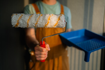 Professional painter gripping paint roller with red handle, standing near blue paint tray,...