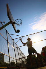 Young guy throws a ball into a basketball hoop on a yard court
