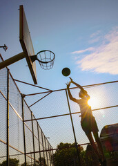 Young guy throws a ball into a basketball hoop on a yard court
