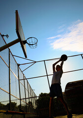 Young guy throws a ball into a basketball hoop on a yard court