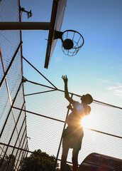 Young guy throws a ball into a basketball hoop on a yard court