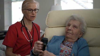 A caregiver and an elderly woman share a moment in a cozy living room, engaging in conversation...