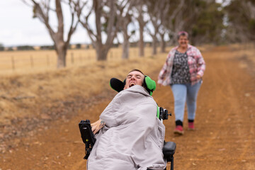 Middle-aged woman running after her son with disability on wheelchair on dirt road