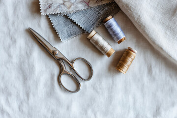 Minimal flatlay of sewing tools: scissors, thread spools, fabric swatches arranged diagonally on white linen surface