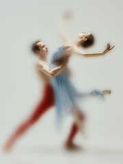 Faded ballet dancer in a pale blue dress is gently lifted by her partner, caught in mid motion with...