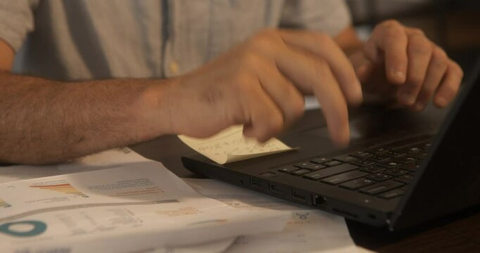 Close-up of a man's hands in front of a laptop checking bills in his living room.