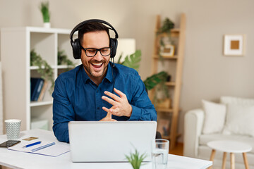 Happy businessman wearing headphones having a video call on laptop and gesturing at home