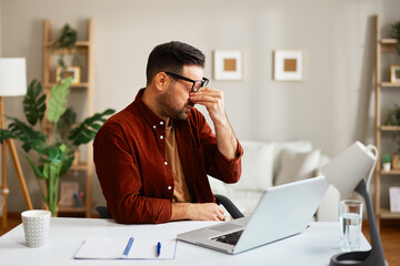 Tired businessman rubbing eyes while working from home office