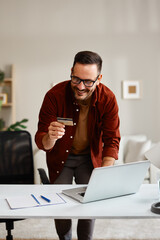 Smiling freelancer making online payment using credit card at home office