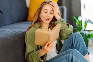 Young woman in glasses enjoying a book sitting on the sofa in a cozy room. Cute woman in glasses...