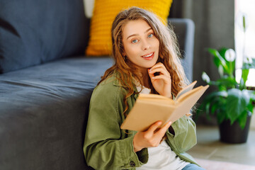 Young woman in glasses enjoying a book sitting on the sofa in a cozy room. Cute woman in glasses...