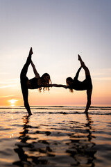 Silhouette of young women standing in gymnastic poses in the water at sunset. Beautiful dancers...