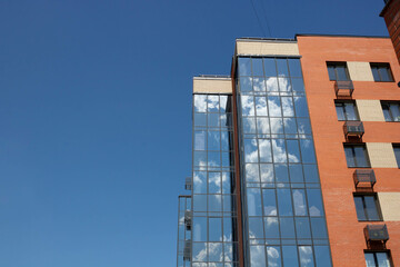The glass facade of the brick building reflects a blue sky with white clouds