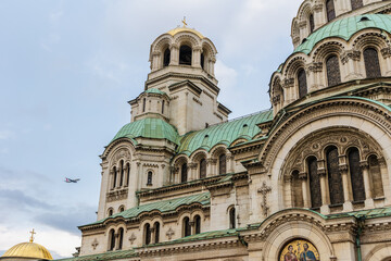 Fototapeta premium Close-Up Side View of Alexander Nevsky Cathedral in Sofia, Bulgaria with Airplane in Sky and Architectural Details of Dome and Arches