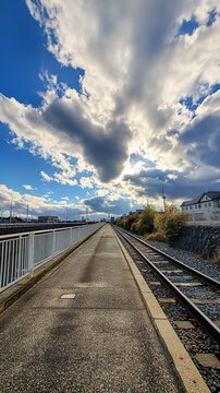 Dramatic sky with sunbeams piercing through clouds over an empty railway platform with parallel tracks and urban landscape in background