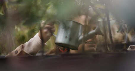 Young woman watering plants with a metal watering can in a lush garden center, showcasing the joy of gardening and plant care
