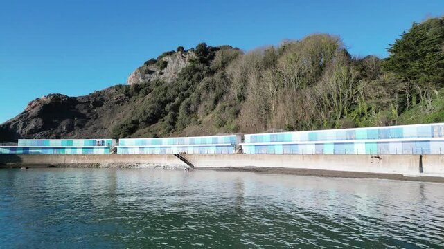 Torquay, Torbay, South Devon, England: DRONE VIEWS: The drone zooms out froma row of colourful beach huts / chalets on Meadfoot beach. Torbay is a popular UK holiday destination