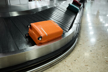 Bright orange suitcase and others waiting on the baggage carousel at a busy airport terminal during...