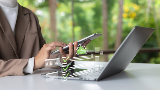 Businesswoman using tablet and laptop with carbon credit icons and green checklists, representing eco-friendly digital business and ESG compliance.
