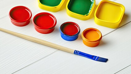 Colorful paint containers and a paintbrush on a white wooden surface