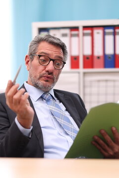 Businessman in black suit has a file and a pen in his hand and is very surprised