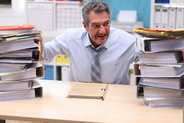 Office worker in shirt and tie sitting in the office next to stacks of files and freaking out