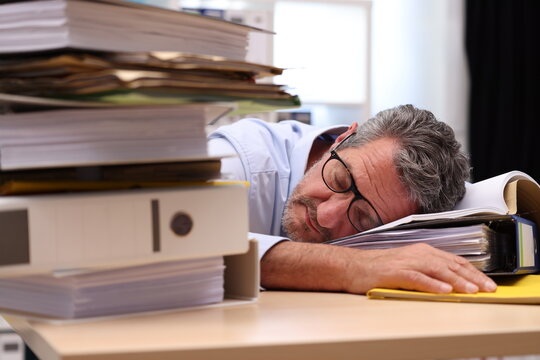 Office worker with glasses sleeping on a file, hand outstretched and files in the foreground