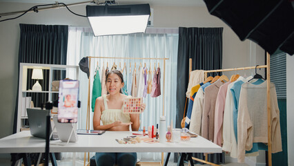 Young beautiful Asia lady blogger look phone camera recording swatch apply eye shadow palette on...