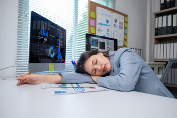 A woman is sleeping on a desk with a computer monitor and papers in front of her