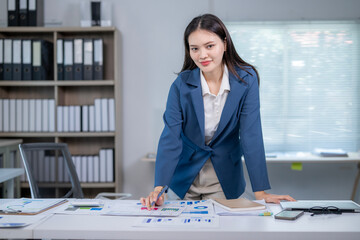 A woman in a blue suit stands at a desk with a white shirt and a pen