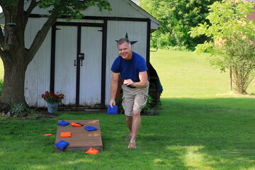 Middle aged man in a blue shirt is throwing corn hole bags during a backyard game © John Outdoors