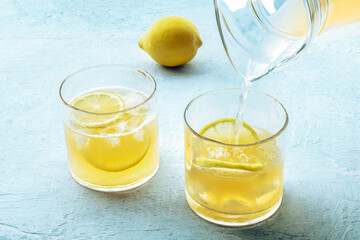 Lemonade poured from a jug into a glass, with a fresh lemon, on a blue slate background