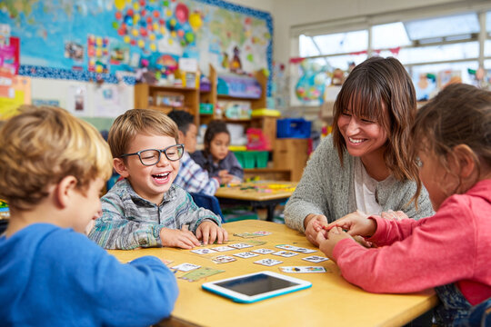 Group of children with special needs smiling and laughing while playing board games in classroom as teacher watches. Inclusive education, joy, and teamwork concept.

