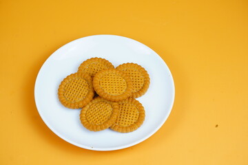 A plate of golden-brown, round, crunchy biscuits with a textured surface, set against an orange background.